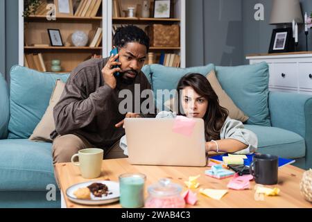 Junge freischaffende gemischte Rassen-Paar Kleinunternehmer, die im Heimbüro an einem Laptop arbeiten, Probleme mit der Internetverbindung oder Firmen-Web-pag Stockfoto