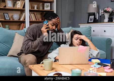 Junge freischaffende gemischte Rassen-Paar Kleinunternehmer, die im Heimbüro an einem Laptop arbeiten, Probleme mit der Internetverbindung oder Firmen-Web-pag Stockfoto