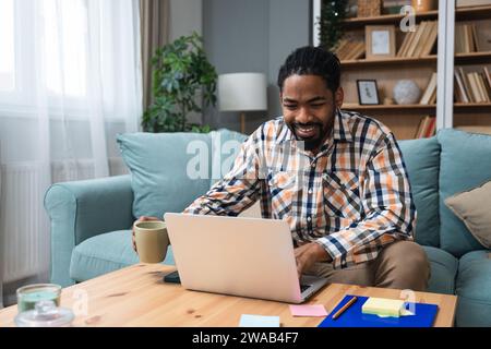 Junger freiberuflicher Geschäftsmann oder Austauschschüler, der von seinem Heimbüro aus auf einem Laptop arbeitet. Afroamerikaner arbeiten an einem neuen Webprojekt uns Stockfoto