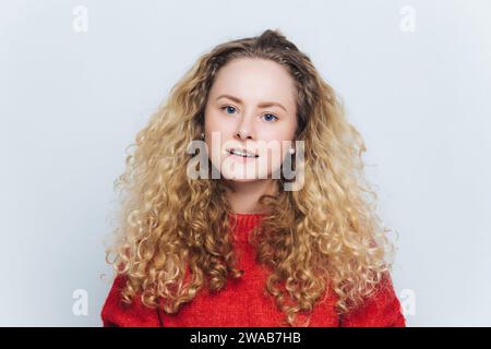 Lebhafte junge Frau mit lockigen blonden Haaren in einem warmen roten Pullover, der Freude und Komfort ausstrahlt Stockfoto