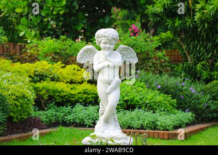 Entzückende freche Cupid-Skulptur in einem frisch grünen Garten Stockfoto