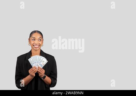 Glückliche junge afroamerikanerin im formellen Anzug zeigt viel Geld Stockfoto