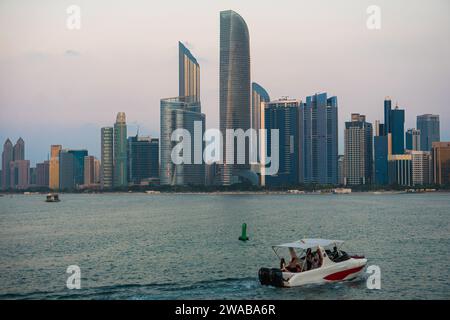 Skyline von Abu Dhabi bei Sonnenuntergang vom Aussichtspunkt Abu Dhabi. Ein Boot mit Leuten, die vorbeifahren. Welthandelszentrum Abu dhabi, das Wahrzeichen Stockfoto