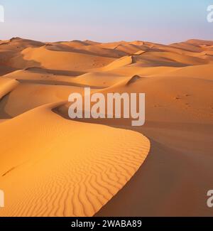 Gekrümmte Sanddünen bei Sonnenuntergang im leeren Viertel, Rub'al Khali Wüste. Orangefarbene Farben Stockfoto