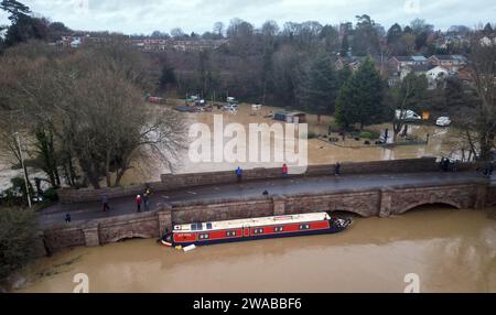 Barrow upon Soar, Leicestershire, Großbritannien. Januar 2024. Wetter in Großbritannien. Ein schmales Boot wird an einer Brücke gefangen, nachdem es sich von seiner Anlegestelle am Fluss Soar befreit hat. Heftiger Regen hat einen großen Teil Großbritanniens heimgesucht, als der kleine, aber potente Sturm Henk traf. Credit Darren Staples/Alamy Live News. Stockfoto