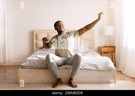 Glücklicher Schwarzer, Der Im Schlafzimmer Aufwacht Und Die Arme Ausdehnt Stockfoto