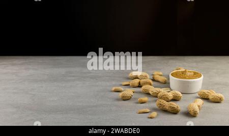 Verstreute Erdnüsse und ein Glas Erdnussbutter auf grauem Hintergrund. Stockfoto