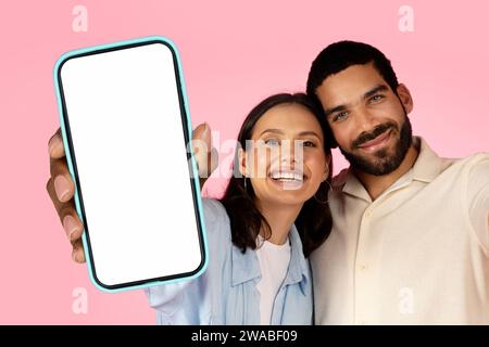 Glückliche Millennials-Mann und -Frau, die großes Handy umarmen und zeigen Stockfoto