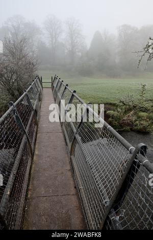 Eine Fußgängerbrücke über den Fluss Arrow in der Nähe von Studley an einem nebeligen Morgen im Winter. Stockfoto