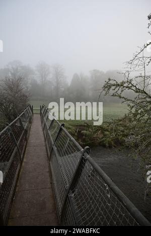 Eine Fußgängerbrücke über den Fluss Arrow in der Nähe von Studley an einem nebeligen Morgen im Winter. Stockfoto