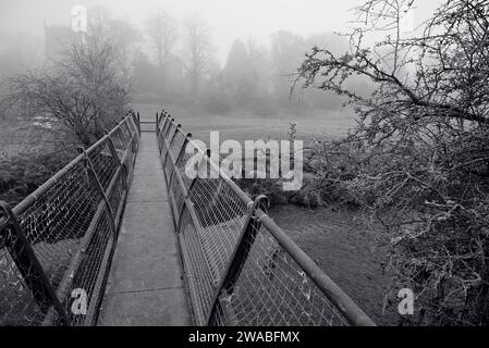 Eine Fußgängerbrücke über den Fluss Arrow in der Nähe von Studley an einem nebeligen Morgen im Winter. Stockfoto