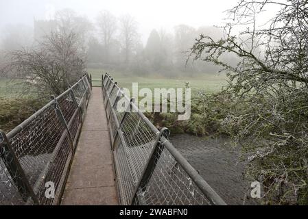 Eine Fußgängerbrücke über den Fluss Arrow in der Nähe von Studley an einem nebeligen Morgen im Winter. Stockfoto