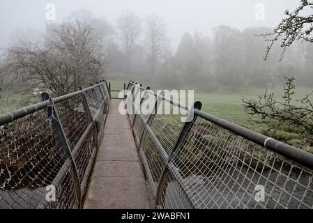 Eine Fußgängerbrücke über den Fluss Arrow in der Nähe von Studley an einem nebeligen Morgen im Winter. Stockfoto