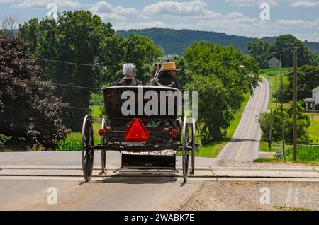 Ronks, Pennsylvania, USA, 23. Juli 2023 - Rückansicht eines amischen Paares in einem offenen Pferd und Buggy, Crossing RR Tracks auf der Landstraße an einem sonnigen Sommertag Stockfoto