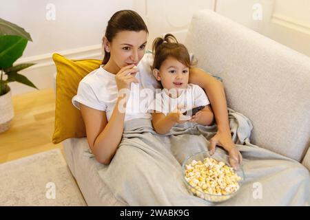 Mom und Tochter schauen mit Popcorn auf dem Sofa fern Stockfoto