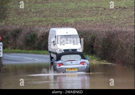 Offenham, Evesham, 3. Januar 2024 – Ein BMW-Fahrer versuchte und scheiterte, durch Hochwasser zu fahren, obwohl ein anderes Fahrzeug bereits auf derselben Strecke verlassen wurde. Der ältere Fahrer drehte seinen Motor auf, als er durchfuhr, aber seine Geschwindigkeit war zu hoch und Wasser stieg in seinen Motor ein. Das Fahrzeug ging schließlich wieder los, aber es kam nur wenige Meter vom Trockenland entfernt zu einer weiteren Haltestelle. Ein Straßenarbeiter kam dann an und legte als letzte Beleidigung ein Schild mit der Aufschrift „Road Closed“ vor sein Fahrzeug. Es geschah neben dem Offenham Caravan Park, der sich in der Nähe von Evesham in Worcestershire befindet, wo der Fluss Avon niederfließt Stockfoto