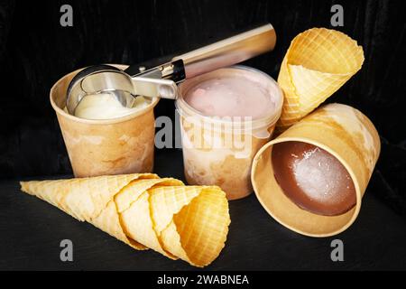 Dieses Bild zeigt drei Tassen Eis in verschiedenen Geschmacksrichtungen: Vanille, Erdbeere und Schokolade. Auf einer der Tassen liegt ein Eislöffel aus Metall Stockfoto