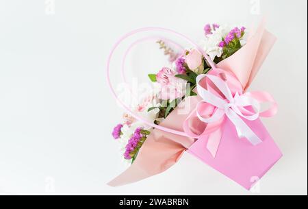 Ein wunderschöner Blumenstrauß, elegant in eine Schachtel mit rosafarbenem Papier gewickelt und mit einem weichen rosa Band gebunden. Unter den Blumen sind Rosen und lilie Stockfoto