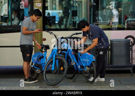 Barcelona, Spanien - 26. Mai 2022: Zwei Teenager asiatischer Herkunft sind dabei, den Elektrofahrraddienst über die Handy-App zu nutzen. Stockfoto