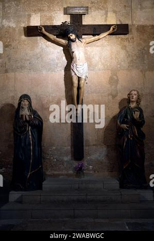 Tarragona, Spanien - 14. Januar 2022: Das Bild Christi am Kreuz, beleuchtet durch ein wenig Licht mit Schatten und am Fuße des Kreuzes zwei Nonnen Stockfoto