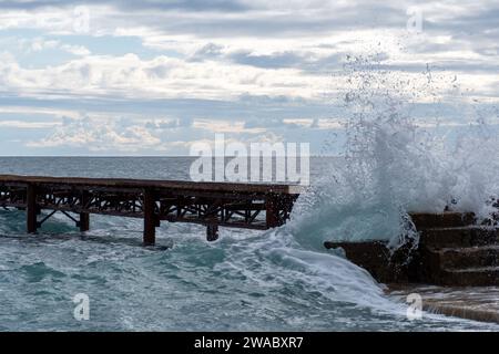 Meereswellen stürzen gegen Pier und Steintreppen unter bewölktem Himmel Stockfoto