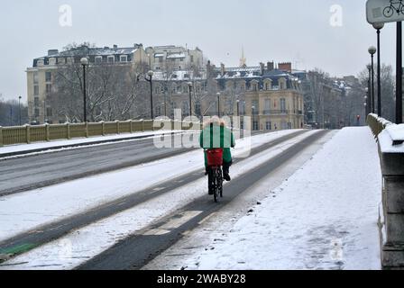 Unerwarteter Schnee in Paris. Eine einsame Frau fährt mit dem Fahrrad entlang der verlassenen Alma-Brücke. Stockfoto