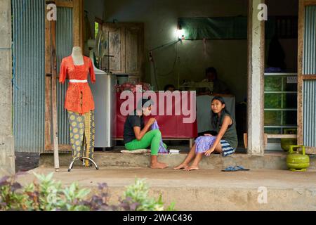 Die Menschen ruhen sich in einem ungewöhnlichen asiatischen Dorf in der Nähe der Straße aus. Kinder spielen und Erwachsene sprechen am Straßenrand. Bali, Indonesien - 12,24 Stockfoto