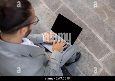Obenliegende Aufnahme eines fokussierten Geschäftsmannes im Anzug, der auf einem leeren Laptop schreibt Stockfoto