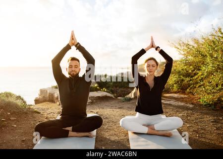 Paare üben Yoga mit Sonnenuntergang Meditation auf dem Küstenweg Stockfoto