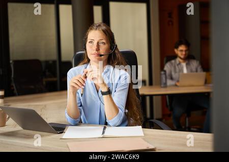Konzentrierte Callcenter-Mitarbeiterin, die in der Nähe ihres verschwommenen männlichen Kollegen wegschaut Stockfoto