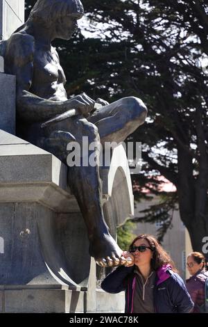 Eine weibliche Touristen küsst den Fuß der Bronzestatue eines Indianerpatagons auf Ferdinand Magellan Monument. Plaza Munoz Gamero aka Plaza de Armas. Punta Arenas. Patagonia. Chile Stockfoto