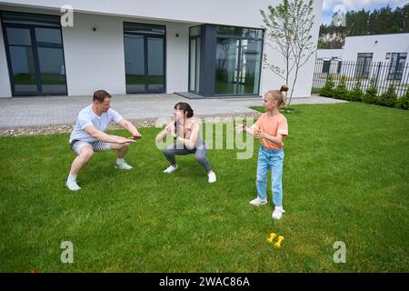 Ein kleines Mädchen, das ihre Mutter und ihren Vater ansieht, wie sie im Garten auf Gras sitzen Stockfoto