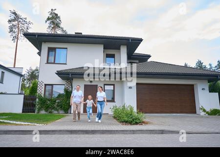Familie hält Hände und rennt an warmen Tagen aus dem neuen modernen Stadthaus draußen Stockfoto