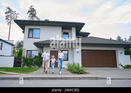 Glückliche kaukasische Mutter, Vater und Tochter, die aus einem neuen, modernen Stadthaus rennen Stockfoto