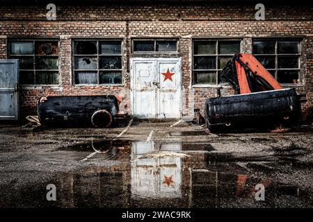 Alte baufällige kommunistische Fabrik mit Ziegelwänden und kaputten Fenstern, eine Tür mit einem roten Stern Stockfoto