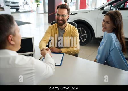 Das Paar kommuniziert mit dem Berater im Bürobereich des Autohändlers Stockfoto