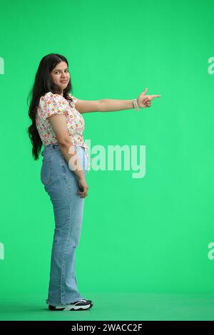 Eine Frau, auf grünem Hintergrund, in voller Länge, zeigt zur Seite, im Profil Stockfoto