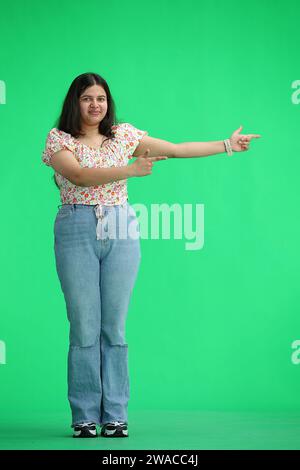 Eine Frau, auf grünem Hintergrund, in voller Länge, zeigt zur Seite Stockfoto