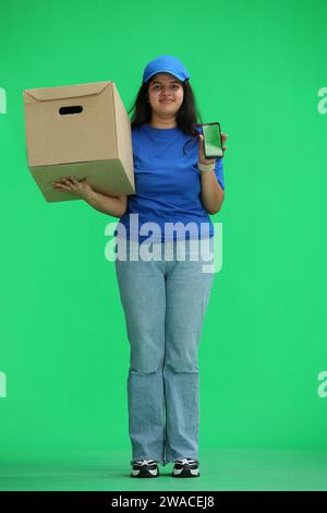 Eine Kurierfrau mit einer Kiste auf grünem Hintergrund, in voller Länge, mit einem Telefon Stockfoto