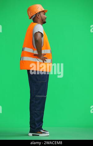 Ein Bauarbeiter auf grünem Hintergrund hält seine Hände am Gürtel, im Profil Stockfoto
