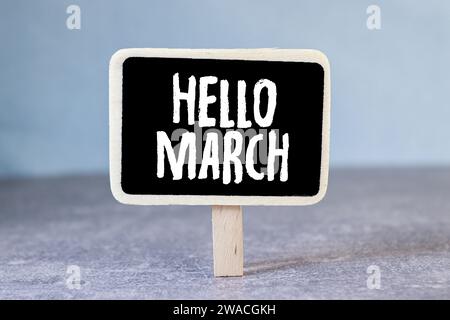 Auf einem hellblauen Holztablett befindet sich eine weiße Tasse Kaffee, ein Griff und eine Serviette, auf der „HELLO MARCH“ steht. Stockfoto