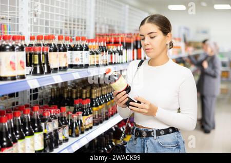 Ein junges Mädchen, das japanische Sojasauce im asiatischen Lebensmittelgeschäft wählt Stockfoto