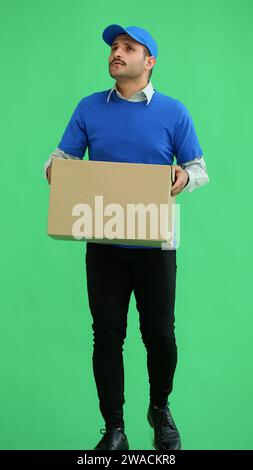 Männlicher Kurier in voller Länge, der eine Kiste auf grünem Hintergrund hält Stockfoto