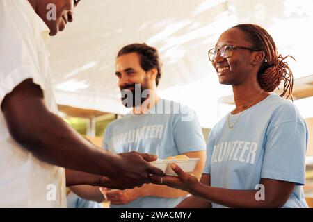 Das wohltätige Team leistet entscheidende Hilfe, indem es Menschen, die in Not sind, gesunde Mahlzeiten liefert. Obdachlose und unglücklichste Person, die von der afroamerikanischen Freiwilligen gedient wurde. Stockfoto