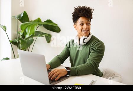Glücklicher Schwarzer Millennials mit schnurlosen Kopfhörern über Laptop Stockfoto