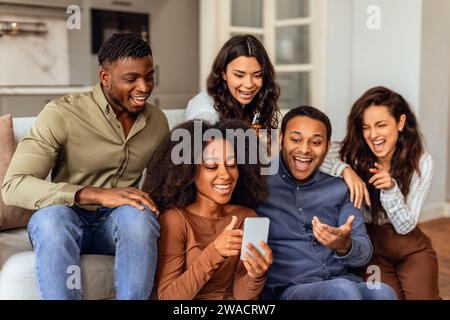 Eine Gruppe multiethnischer Freunde, die durch das Smartphone scrollen, versammelte sich in der Küche Stockfoto