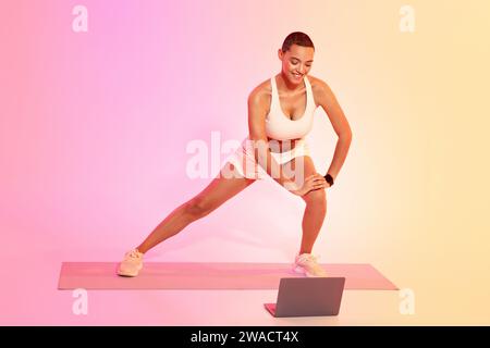 Eine fokussierte Frau mit einem rasierten Kopf dehnt sich auf einer Yoga-Matte in einem seitlichen Ausfallschritt Stockfoto