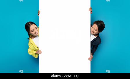 Asiatische Männer und Frauen schauen spielerisch um ein großes weißes vertikales Banner Stockfoto