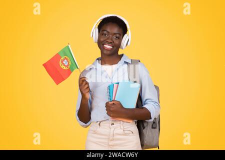 Glückliche Teenager-afroamerikanische Studentin in kabellosen Kopfhörern, mit Büchern Stockfoto