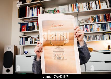Paris, Frankreich - 20. Dezember 2023: In einem luxuriösen Wohnzimmer mit Vitsoe-Regalen und einem hifi-Lautsprecher liest eine Frau eine Finanzzeitung mit einer Cartier-Ringanzeige Stockfoto